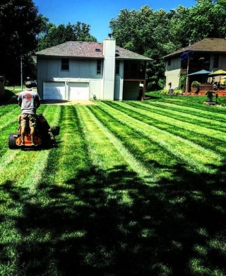 A Pro Mow employee mowing a lawn. The grass is green and shows striping. 